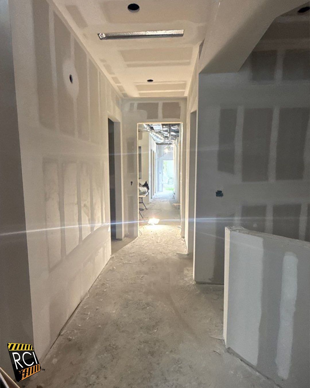Interior hallway under construction, drywall installed on walls and ceiling.