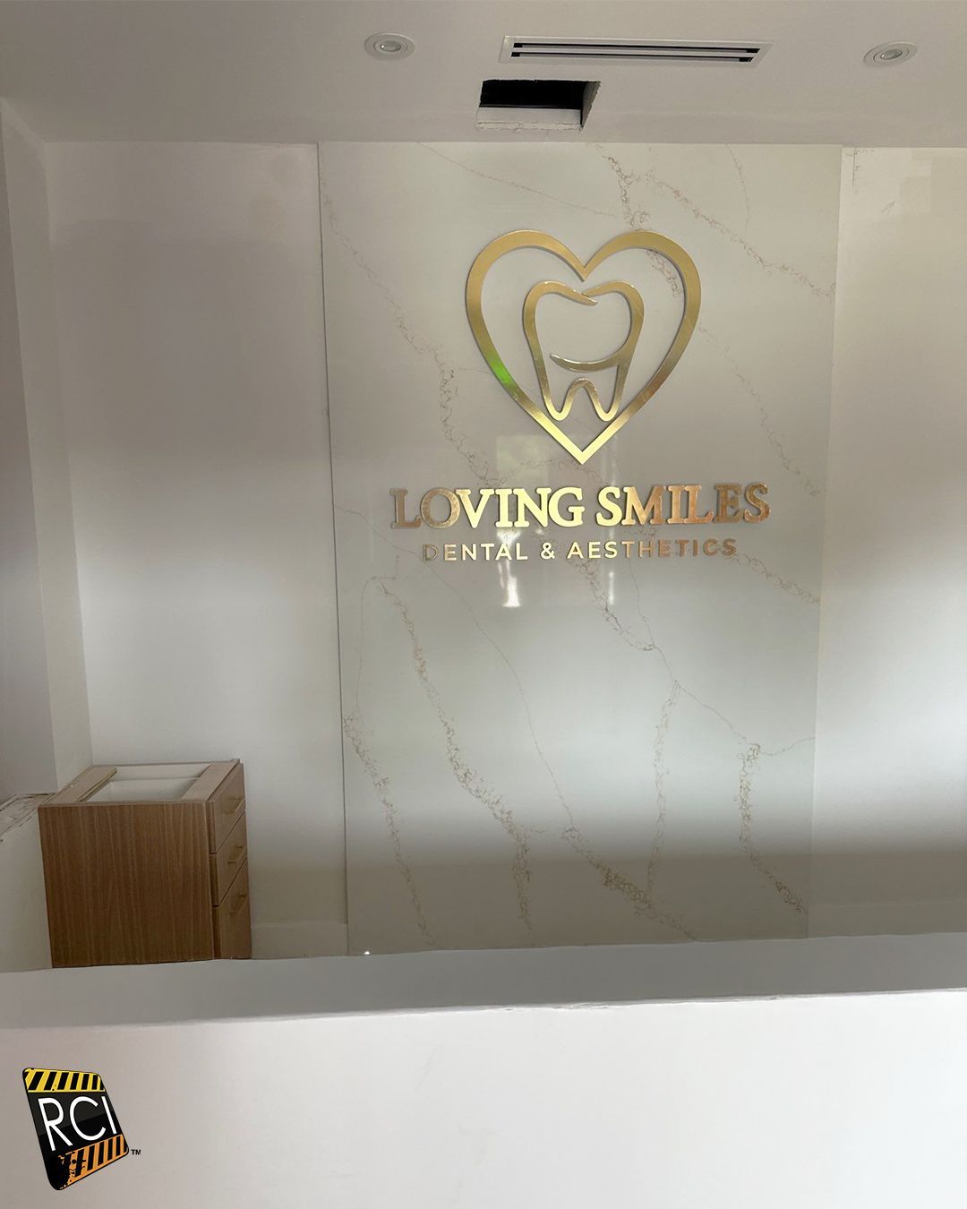 Reception area with gold logo: heart around tooth, "Loving Smiles Dental & Aesthetics" on marble wall.