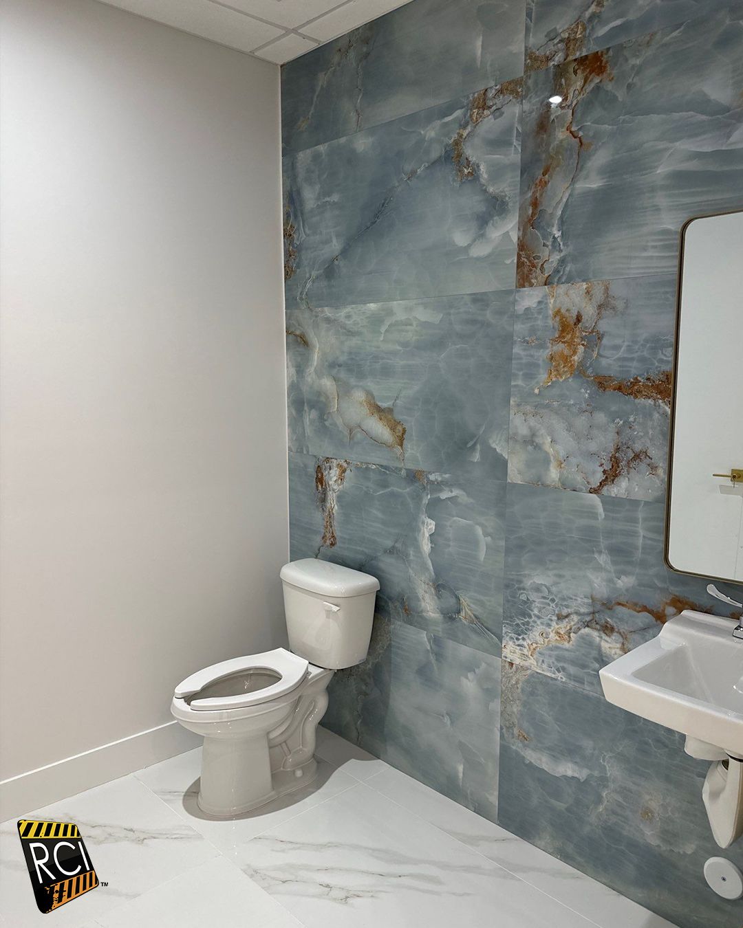 A small bathroom with a white toilet, sink, and blue marble tile wall. White walls and floor.