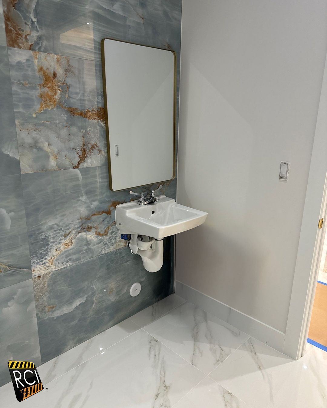 Wall-mounted sink and mirror in a bathroom with blue and white marble-patterned walls and floor.