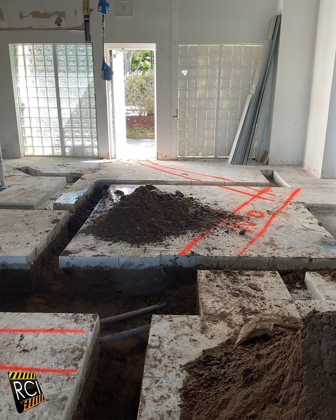 Construction site: Excavated floor with dirt, concrete slabs, and open doorway. Red markings guide work.