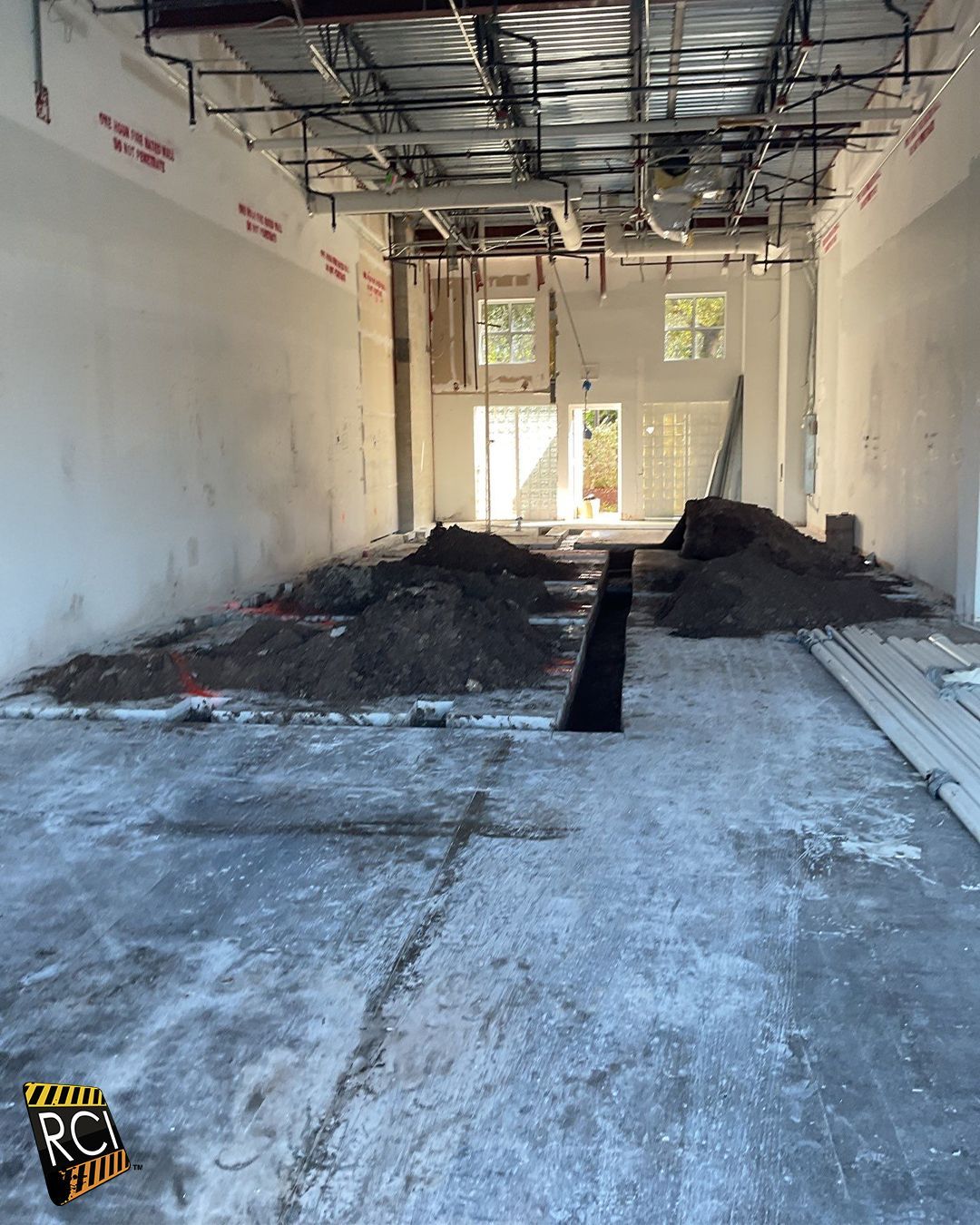 Interior construction site; piles of dirt, concrete floor, exposed pipes and ceiling.