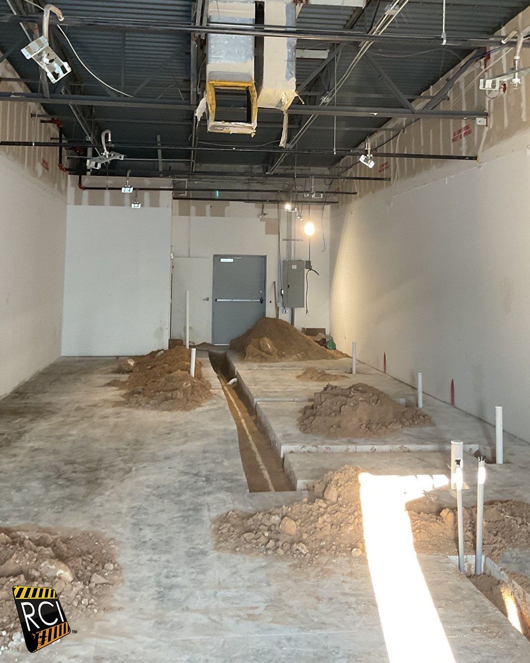 Interior construction site with piles of dirt, trenches, pipes, and exposed ceiling infrastructure.