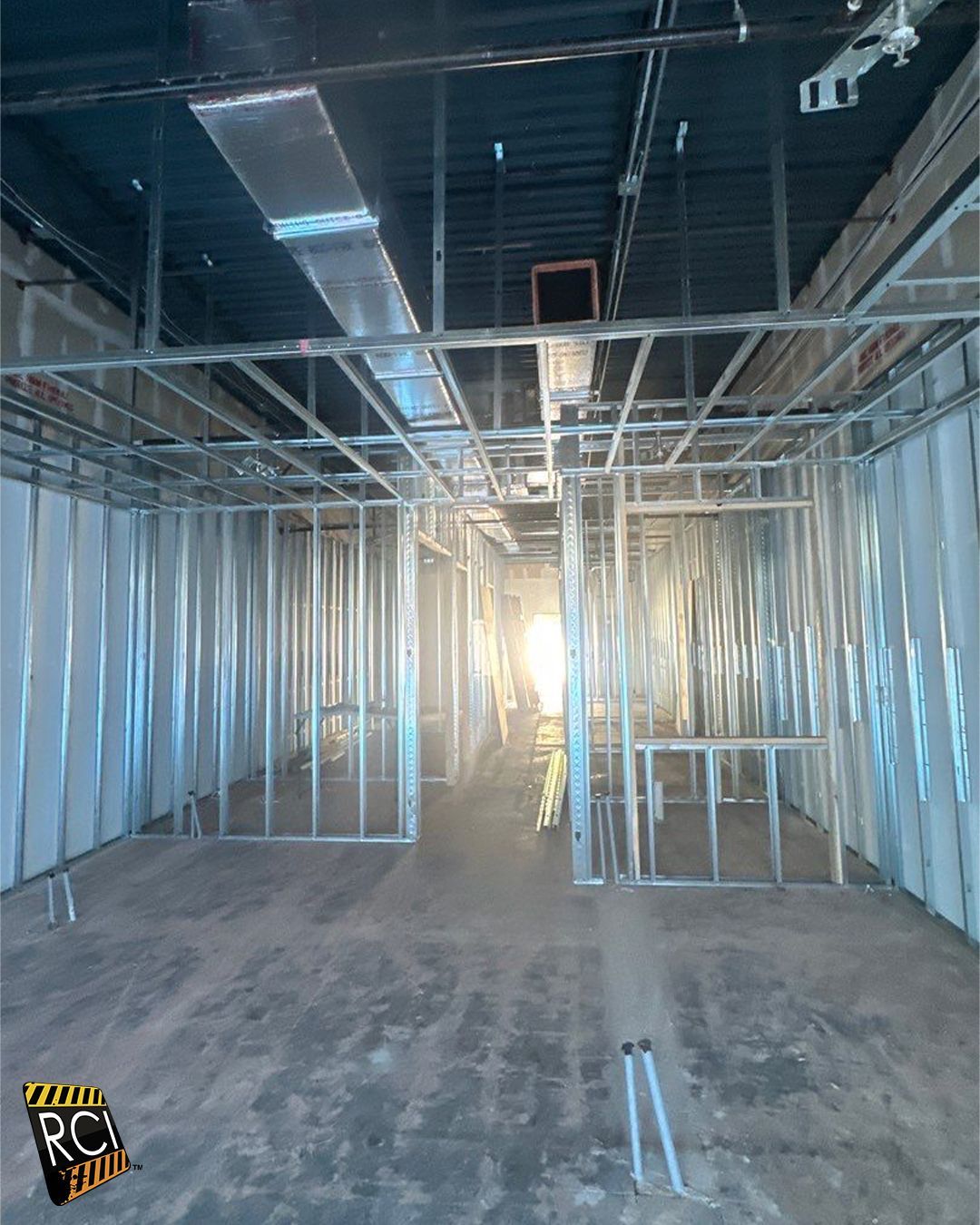 Interior under construction, metal framing of walls and ceiling. Sunlight at end of hallway.