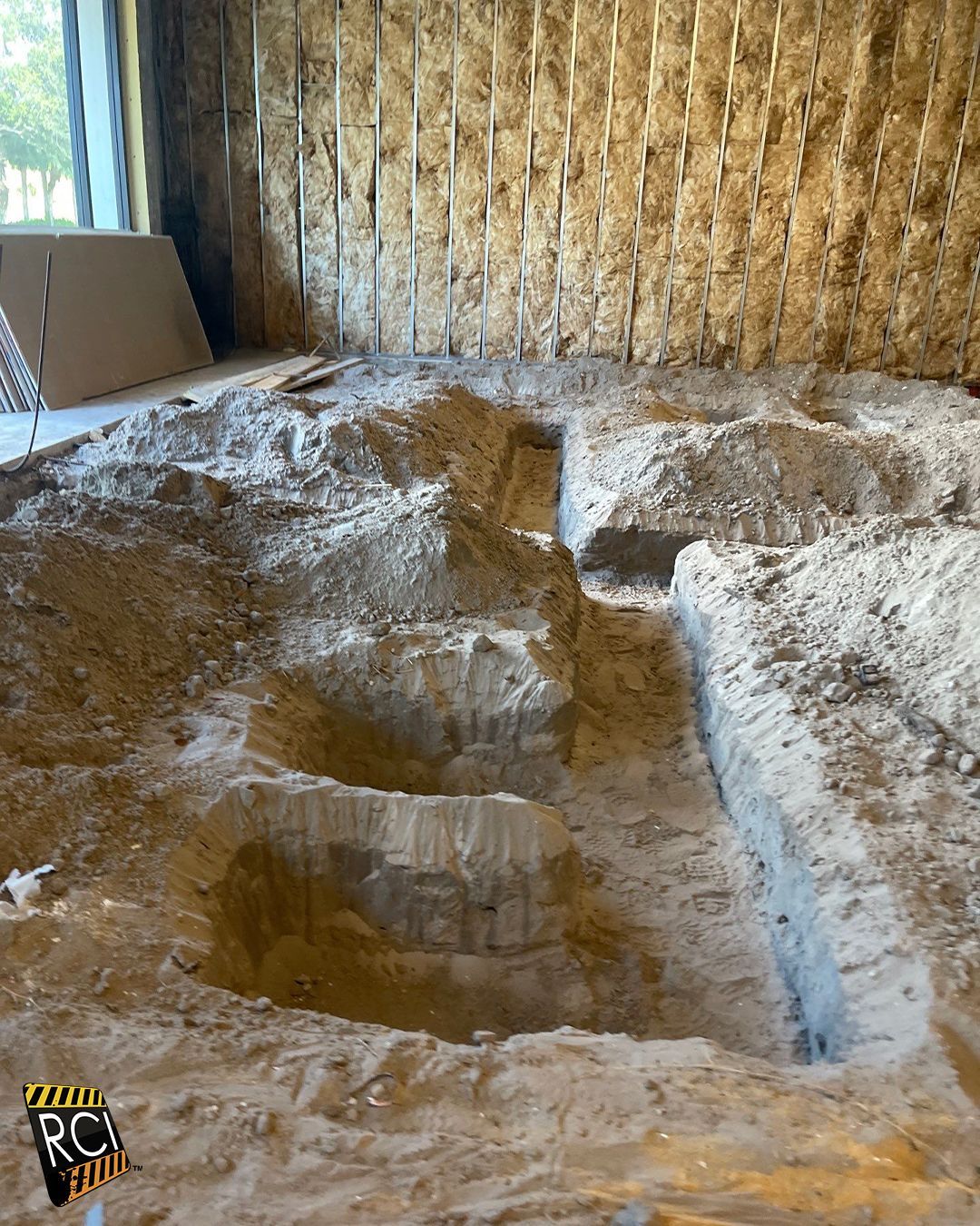 Interior of a construction site with trenches dug into the sandy floor. Wooden walls and insulation visible.
