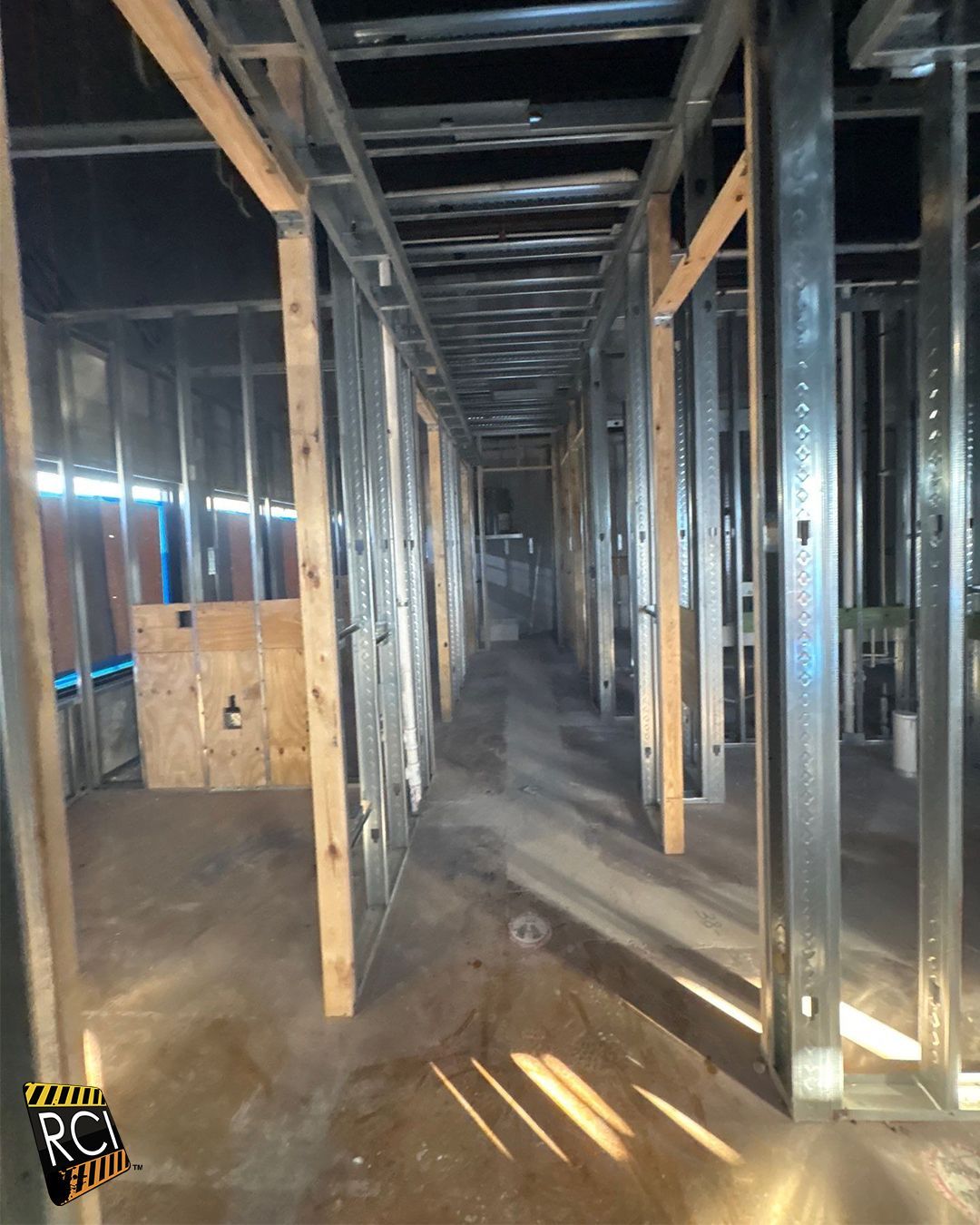 Interior view of metal stud framing for a long hallway. Partially constructed walls with wooden supports and bare concrete floor.