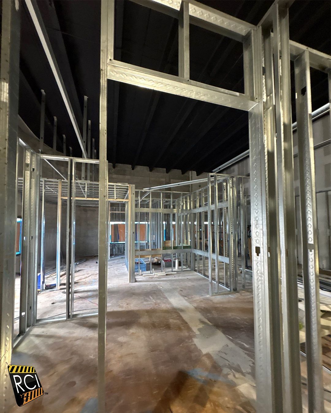 Metal stud framing of interior walls in a construction site with a dark ceiling and light floor.