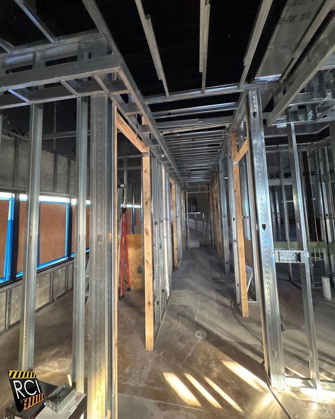 Interior construction: metal studs frame hallway, wood door frames, unfinished ceiling, concrete floor.