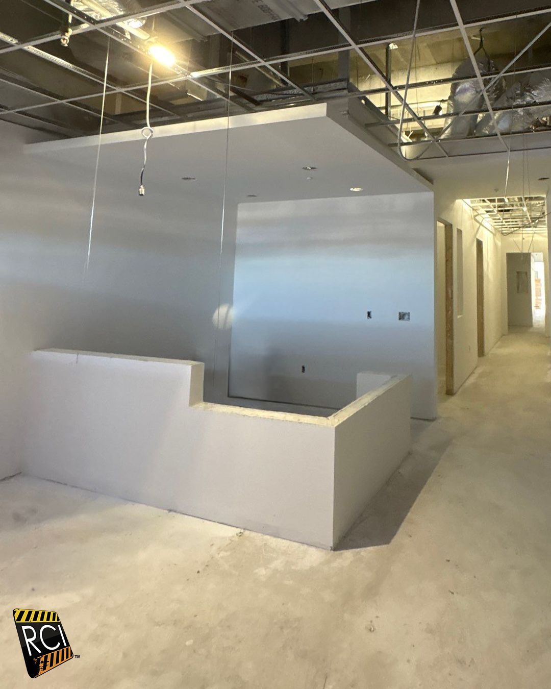 Construction site: white walls and ceiling, partial reception desk, hallway with doorways.