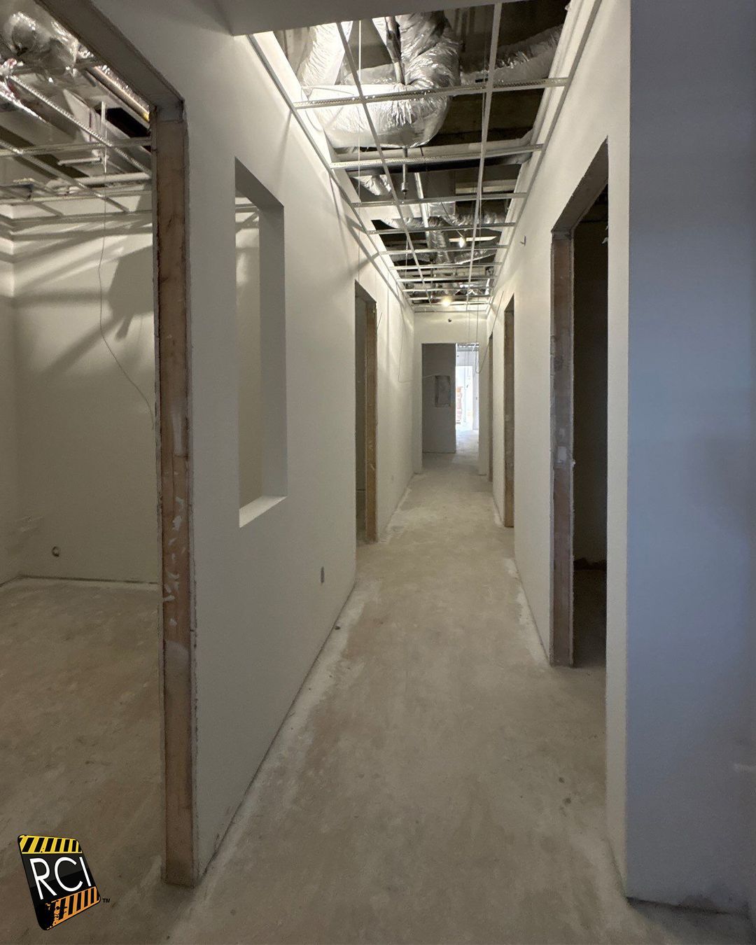 Long hallway under construction, drywall, open doorways, exposed ceiling grid.
