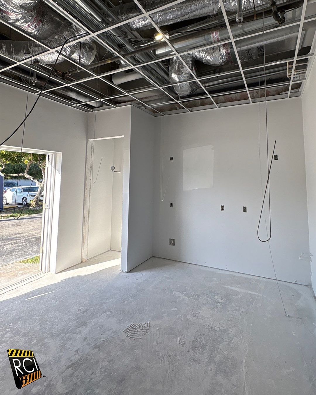 Interior construction site with gray walls and ceiling, exposed ductwork, doorway, and unfinished concrete floor.