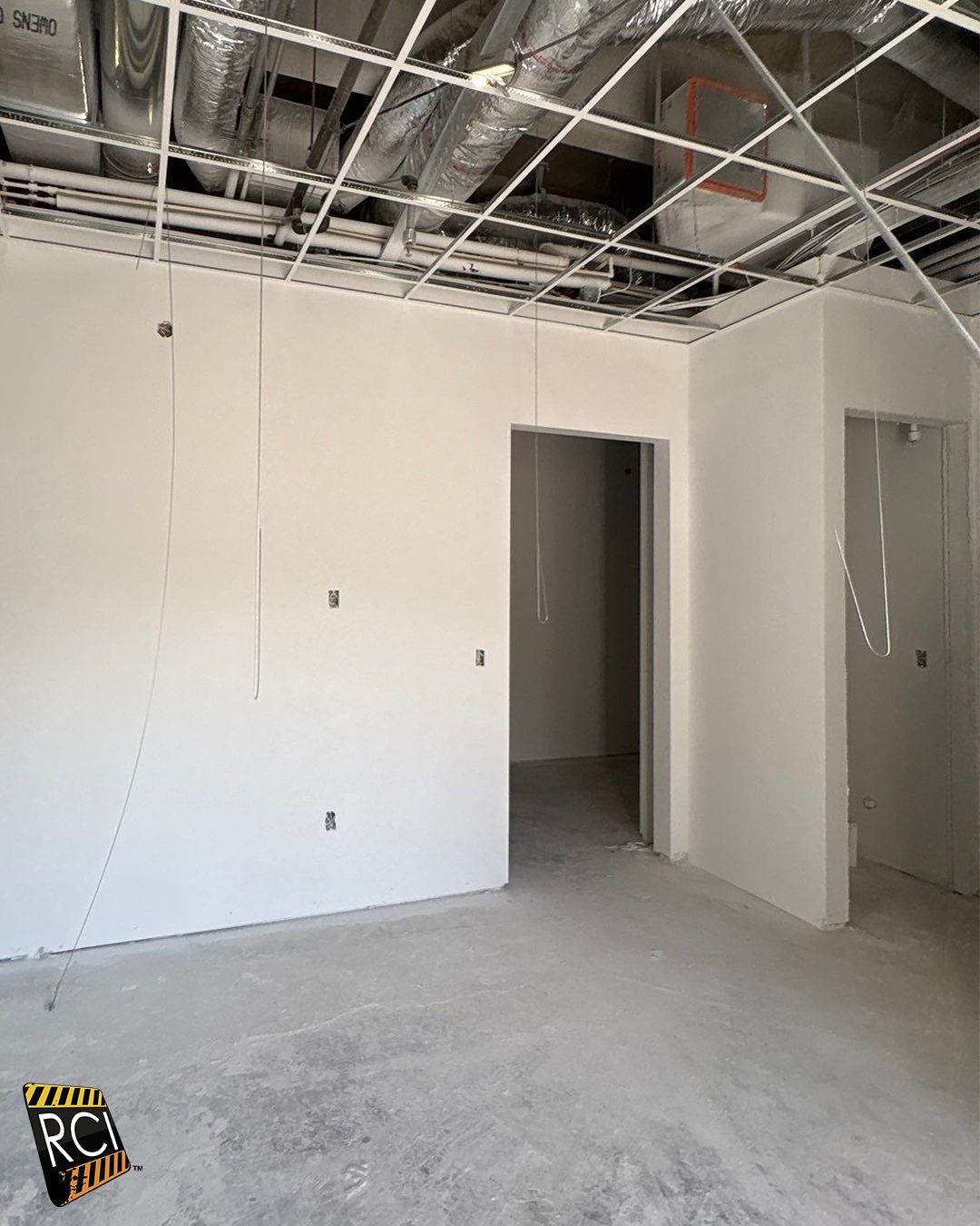 Interior of a room under construction, with white walls, unfinished ceiling, and concrete floor.