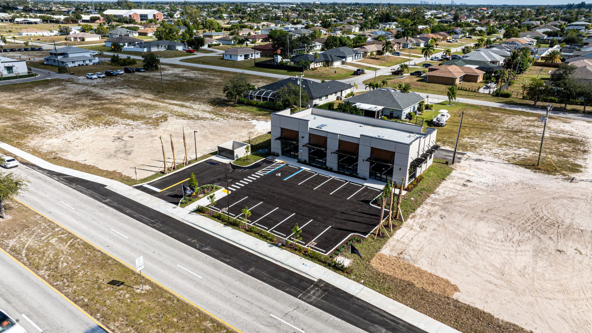 Aerial view of a modern building with a parking lot and surrounding residential area on a sunny day.