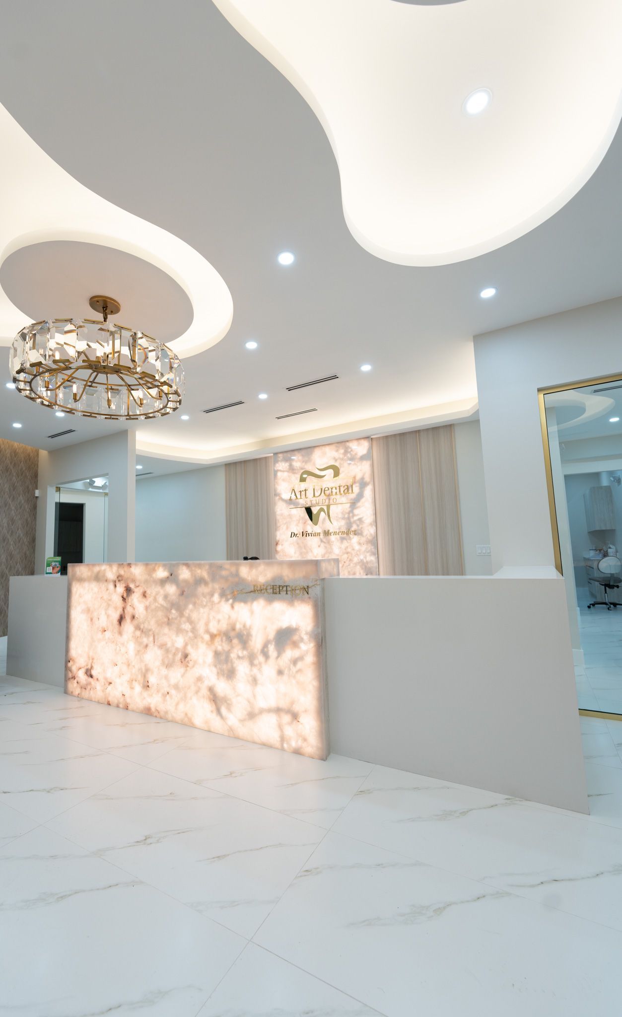 A reception desk in a white room with a chandelier hanging from the ceiling.