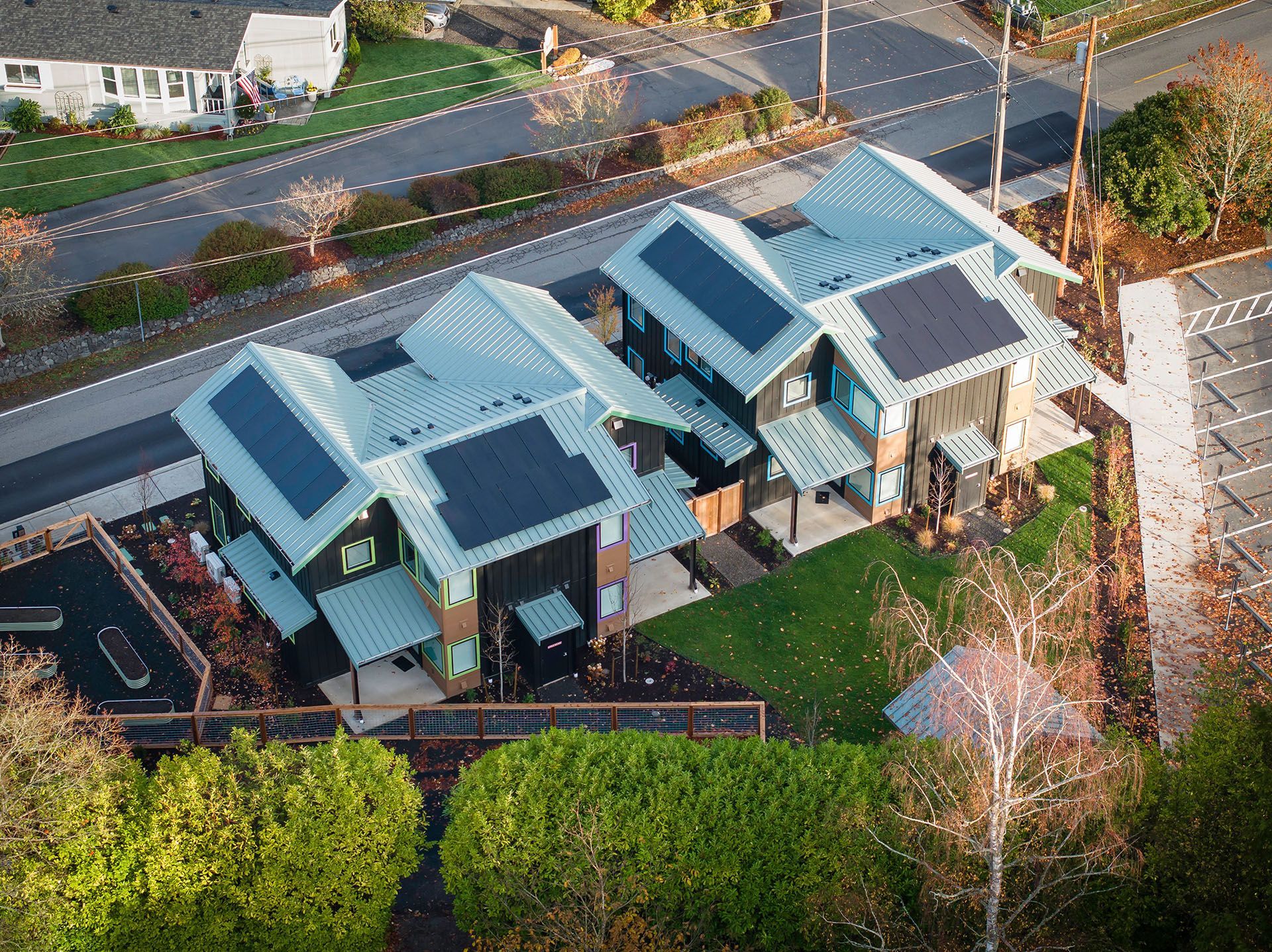Row of colorful houses along a street, with people walking and cycling. Trees and sky in the background.