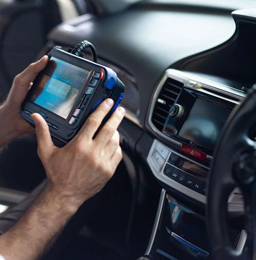 Hands holding a rugged tablet inside a car, viewing a dashboard display.