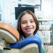 A young girl is smiling while sitting in a dental chair