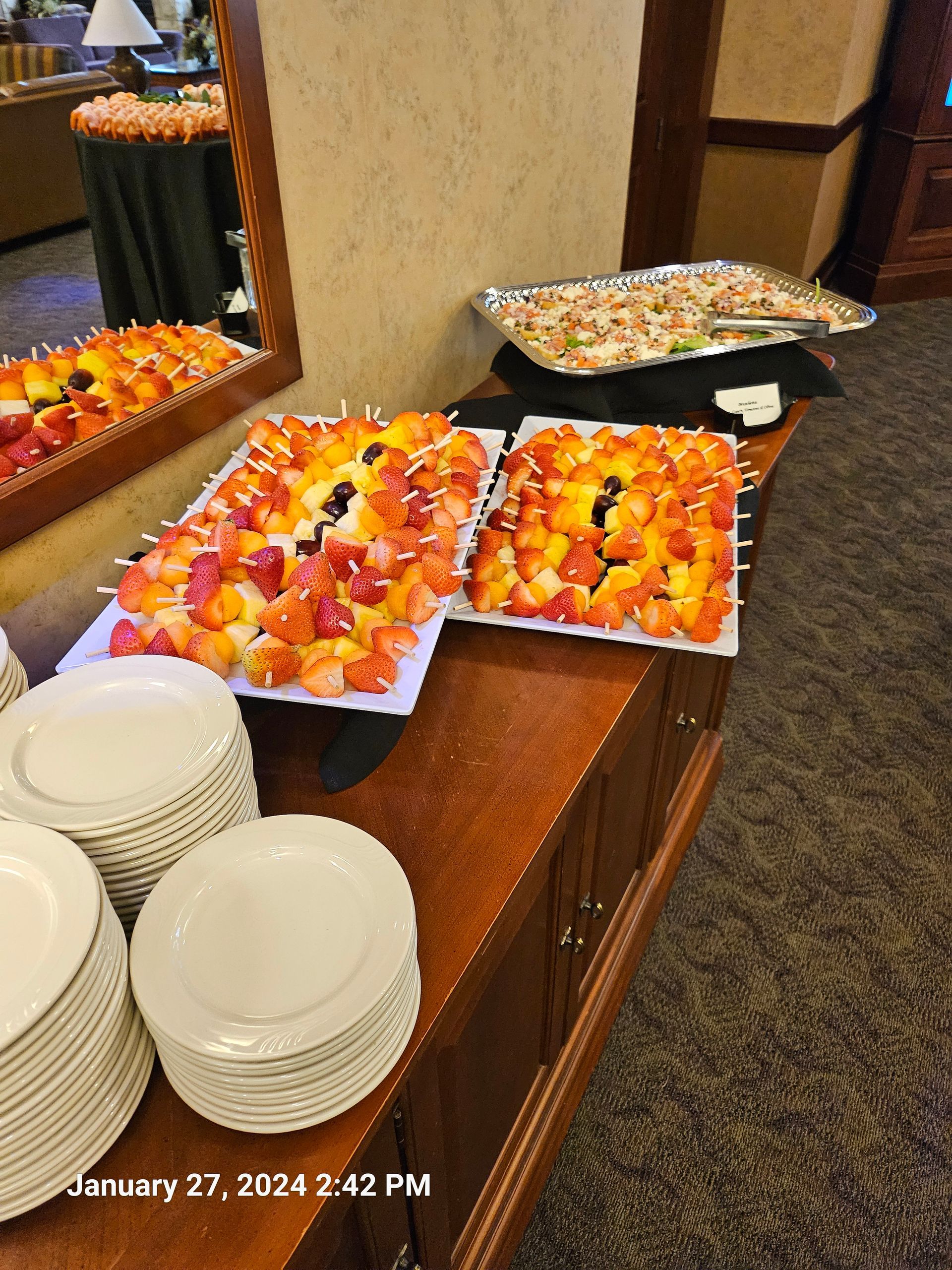 A buffet table with plates and trays of fruit on it.