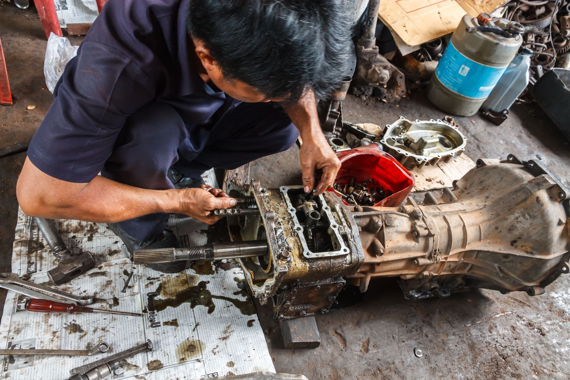 Mechanic repairing a greasy car transmission on the floor in a workshop