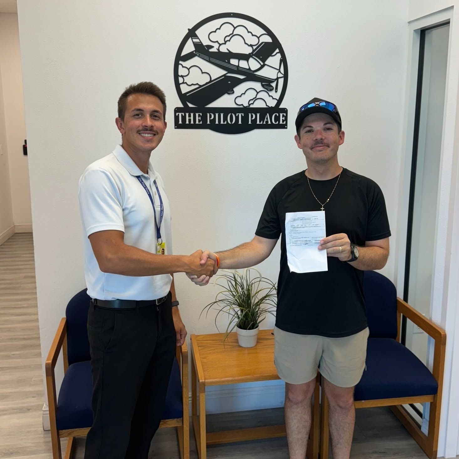 Two men shaking hands in an office lobby; one holds a paper in front of The Pilot Place sign.