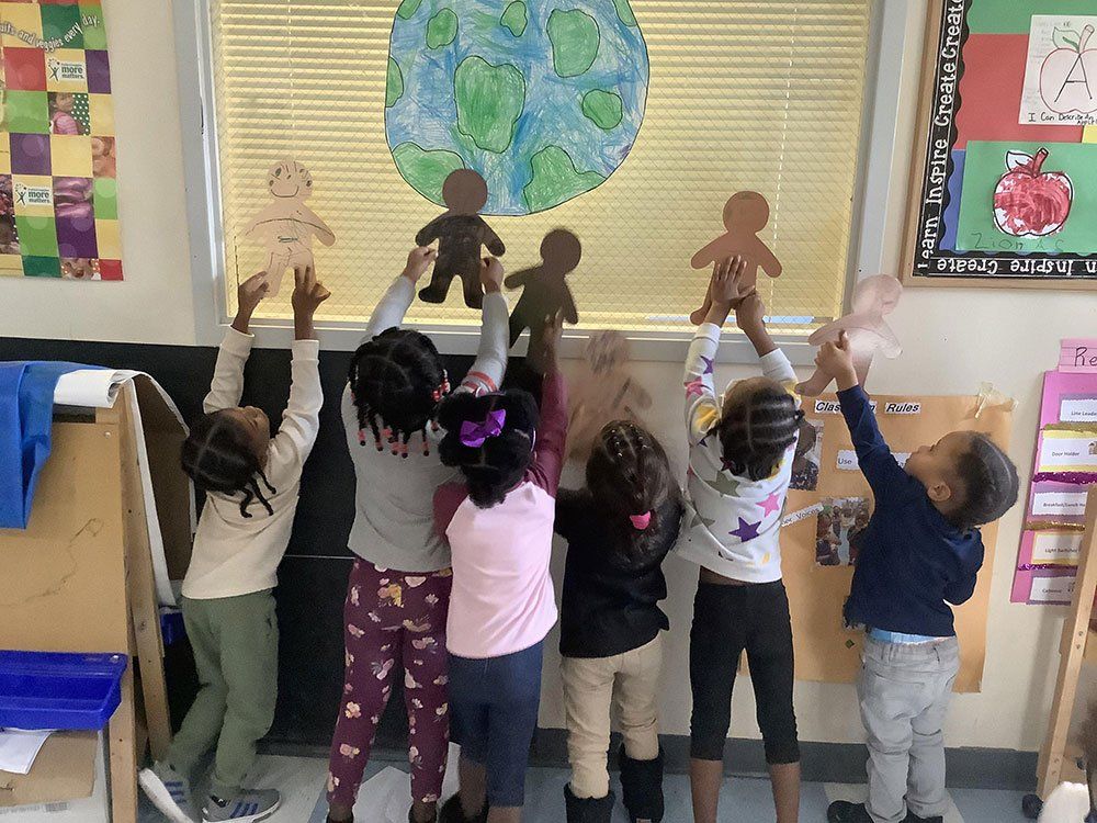 A group of children are holding up gingerbread men in front of a globe