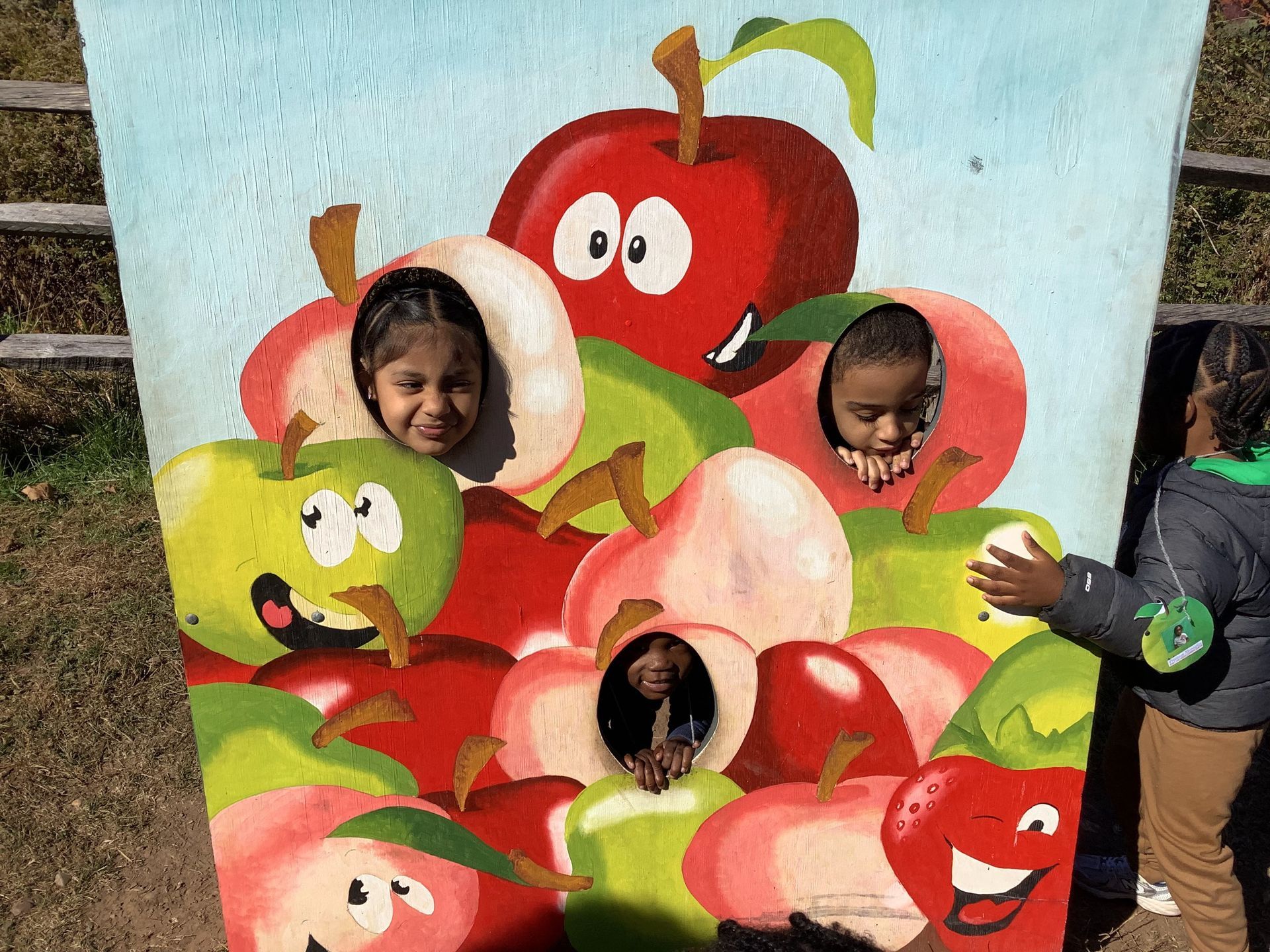 Two children are standing in front of a painting of apples with cartoon faces on them