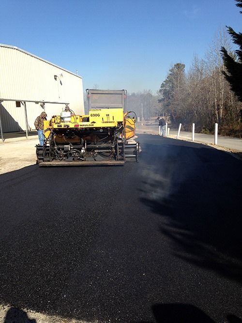 A yellow truck is paving a parking lot in front of a building