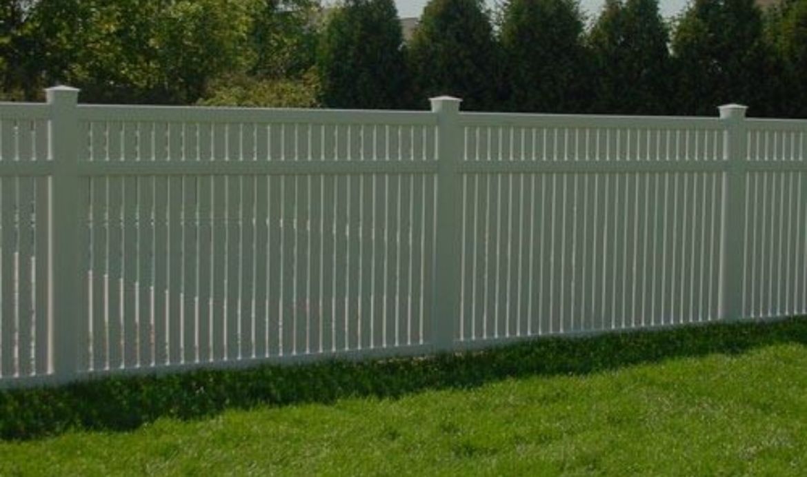 White vinyl fence along a grassy yard with trees in the background