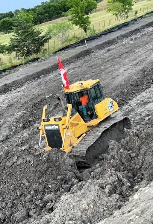 A bulldozer is driving down a dirt road next to a canadian flag.