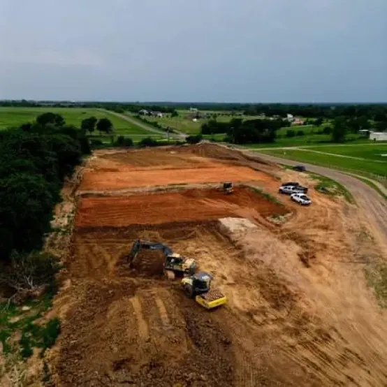 An aerial view of a construction site with a lot of dirt and trees in the background.