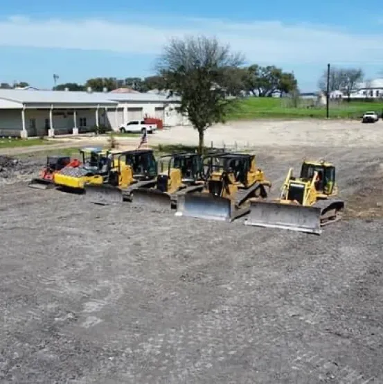 A row of bulldozers are parked in a dirt field.