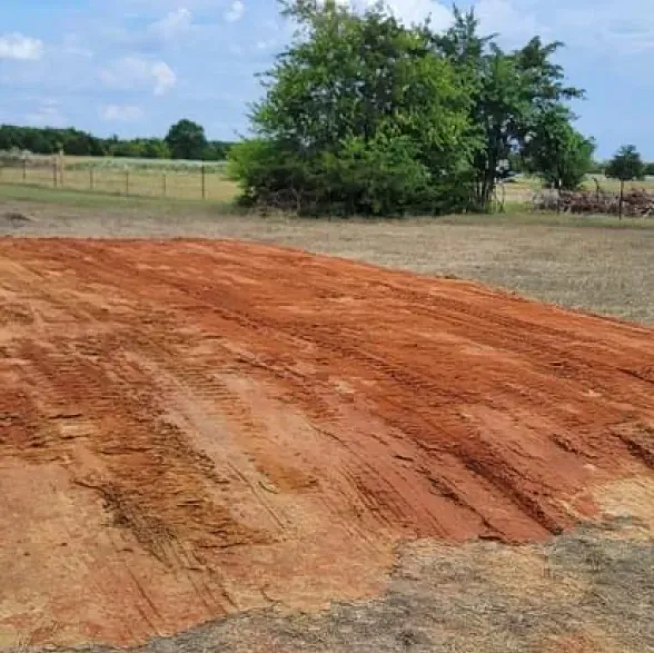 A large pile of dirt in a field with trees in the background.