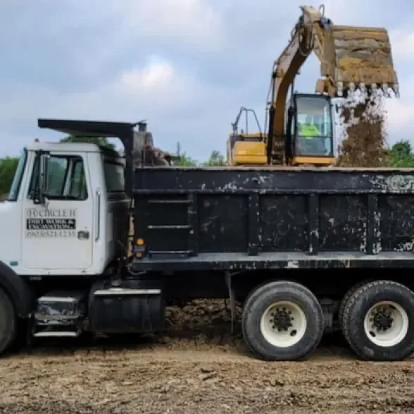 A dump truck with a yellow excavator on top of it