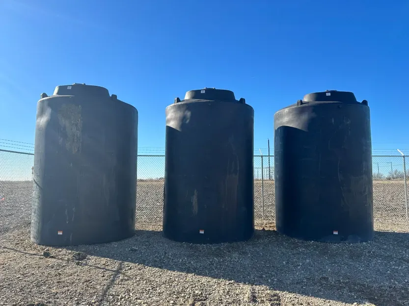 Three black water tanks are lined up in a gravel area.