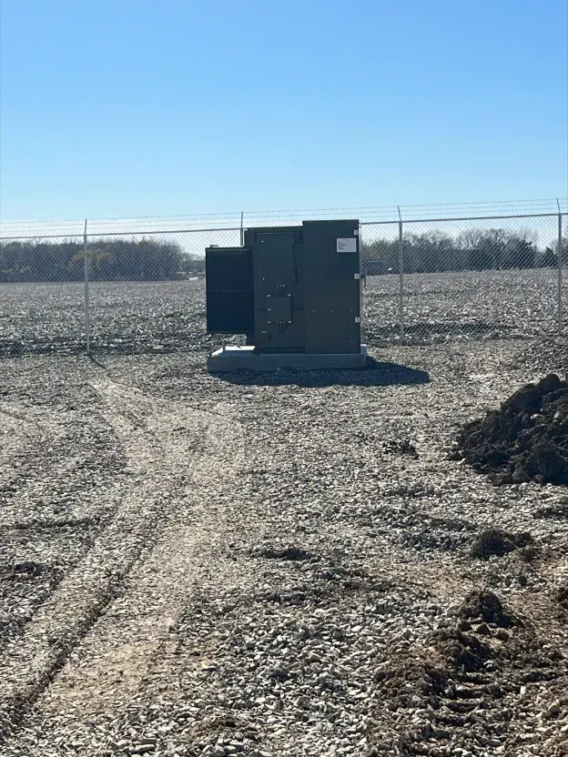 A small building is sitting in the middle of a dirt field next to a chain link fence.