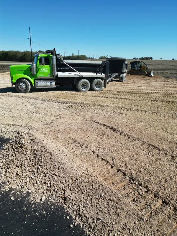 A green dump truck is parked in a dirt field.