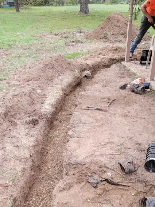 A man is digging a trench in the dirt in a yard.