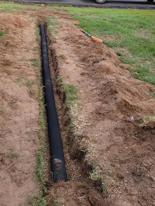 A large black pipe is sitting in the dirt next to a grassy area.