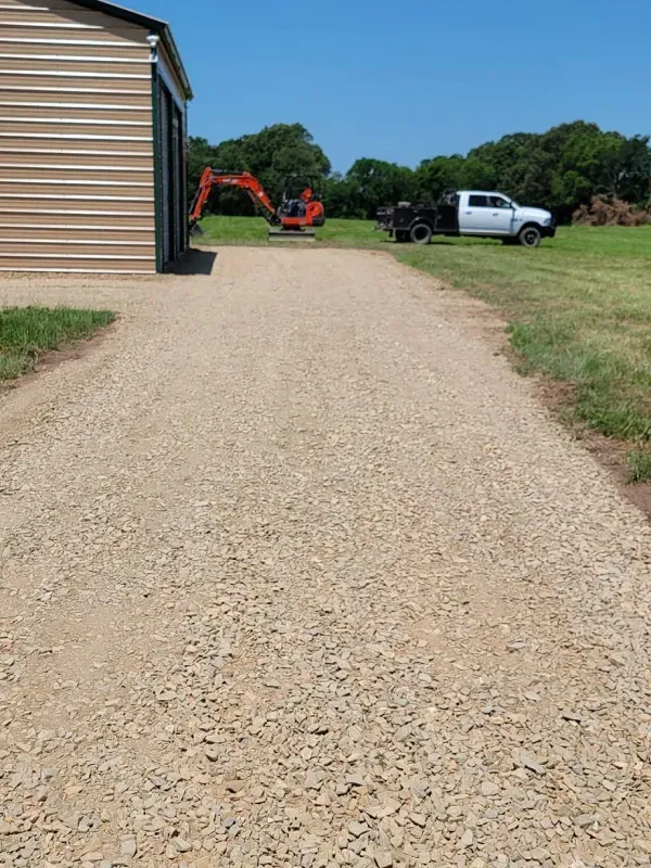A gravel driveway leading to a shed and a truck.