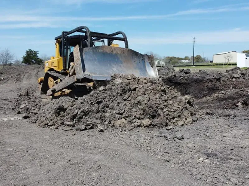 A bulldozer is moving a pile of dirt in a field