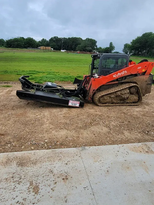 A bulldozer is parked in a dirt lot next to a grassy field.