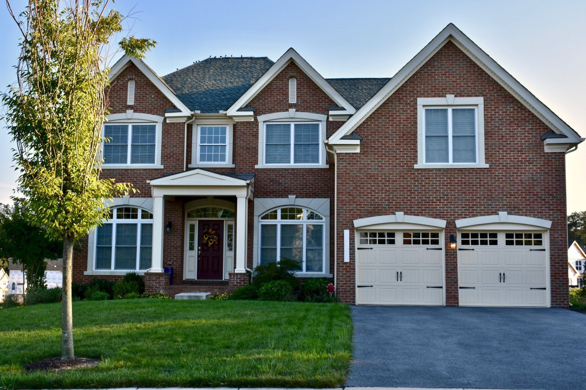 Two-story brick suburban house with white trim, front lawn, and two-car garage