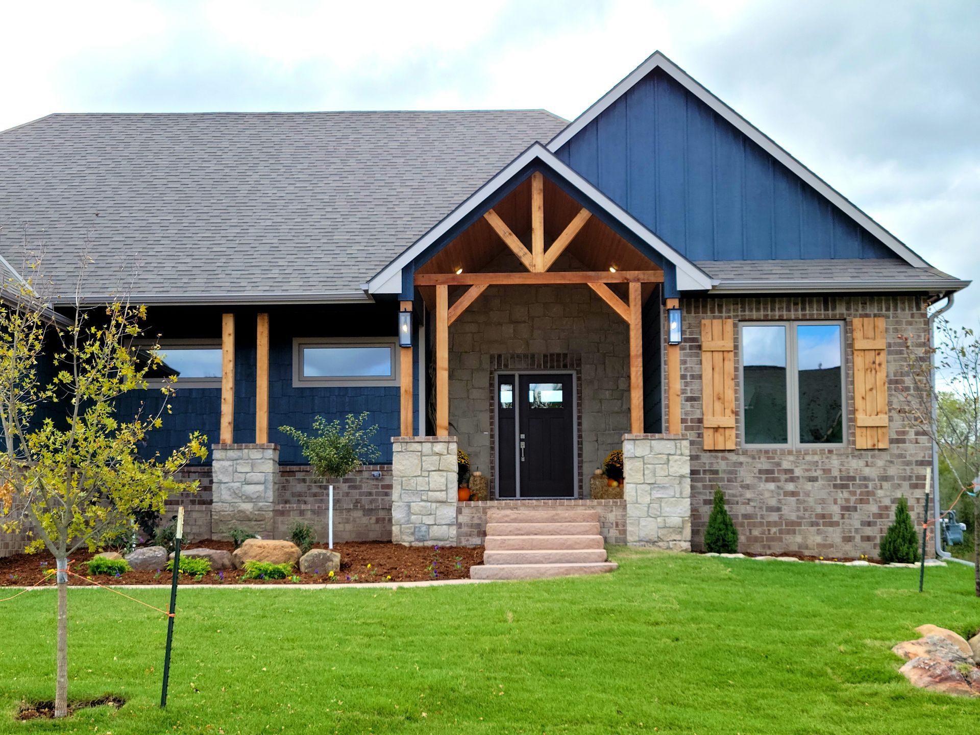 Modern house with blue siding, stone accents, and a front porch on a green lawn