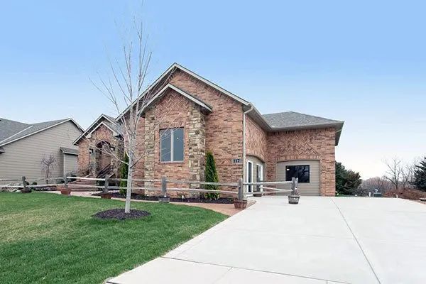 Brick suburban house with a large driveway, green lawn, and clear blue sky