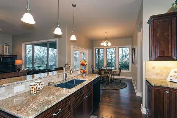 Bright modern kitchen with granite island, dark wood cabinets, pendant lights, and dining area beyond.
