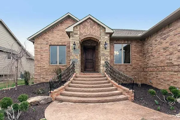 Brick house with arched front entry, wide steps, and black iron railings in a landscaped yard