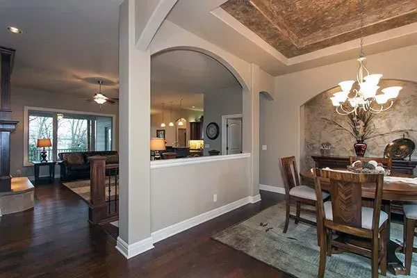 Elegant dining room with chandelier, arched pass-through, dark wood floors, and adjacent kitchen/living area