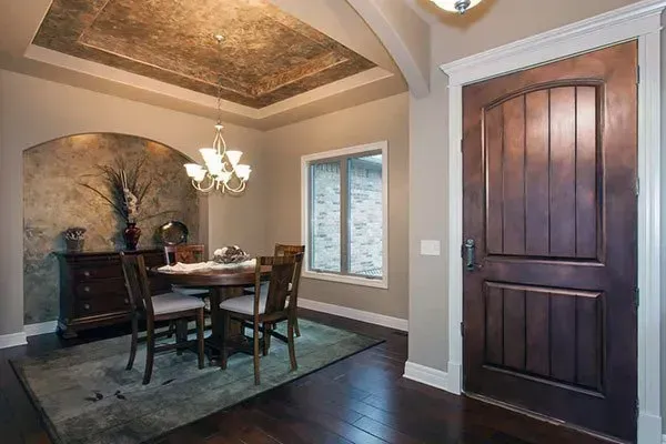 Dining room with dark wood floor, table and chairs, arched ceiling, and tall wood door with window