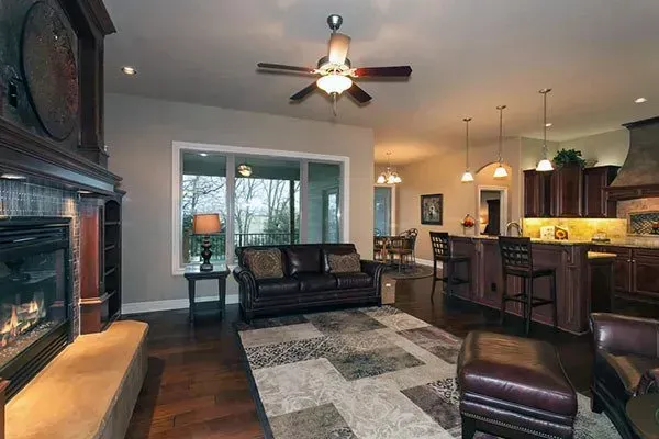 Modern open-concept living room with fireplace, gray sectional, kitchen island, and ceiling fan under warm lighting