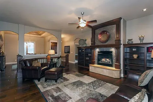 Spacious living room with dark leather furniture, fireplace, patterned rug, and open kitchen view